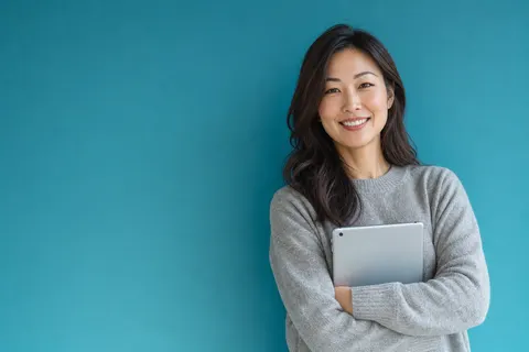 A real estate agent in a grey sweater holding a tablet against a teal wall