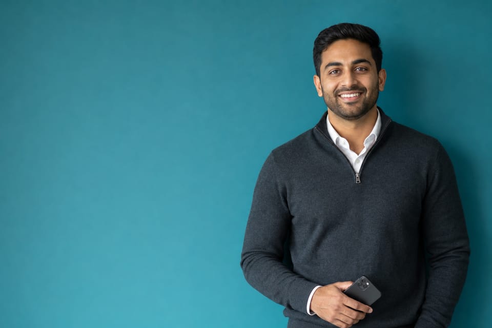 A newly licensed real estate agent in a charcoal sweater holding a phone against a teal wall